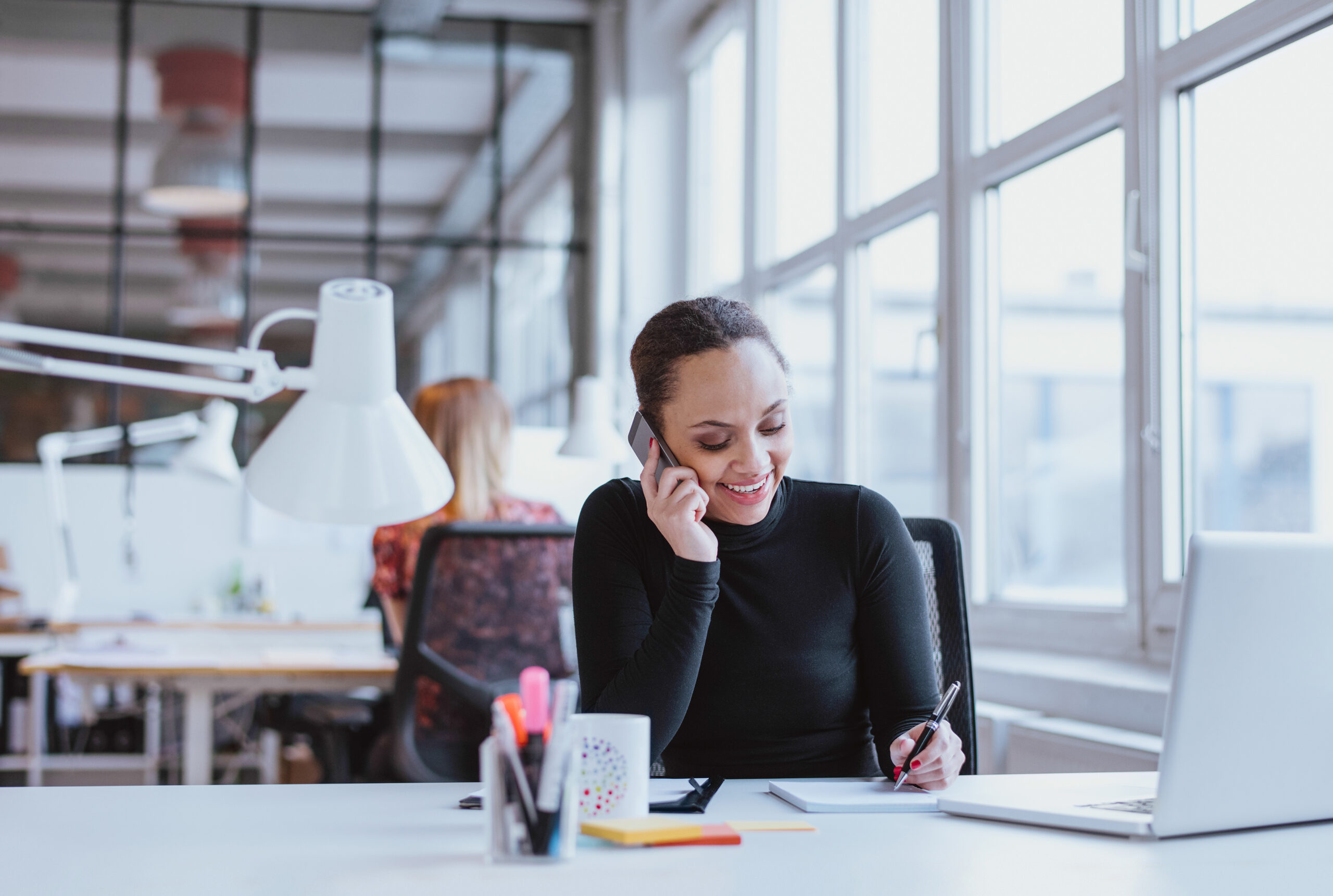 Happy,Young,Woman,Taking,Notes,While,Talking,On,Mobile,Phone.